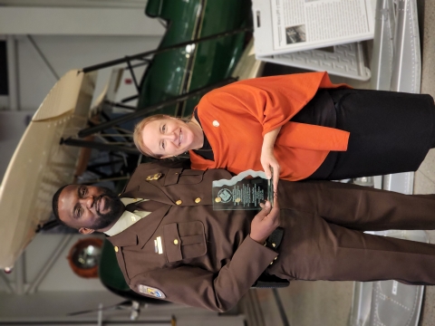 A man and a woman pose with an award in front of an airplane
