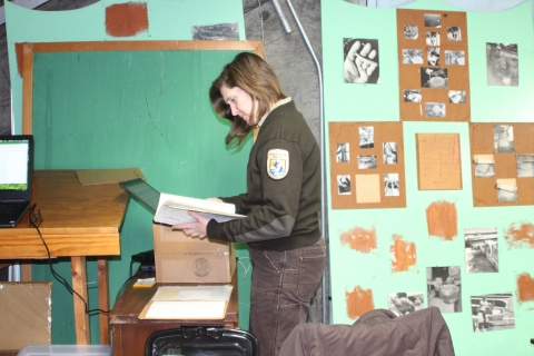 A woman in Service uniform stands looking through files in a storage space.