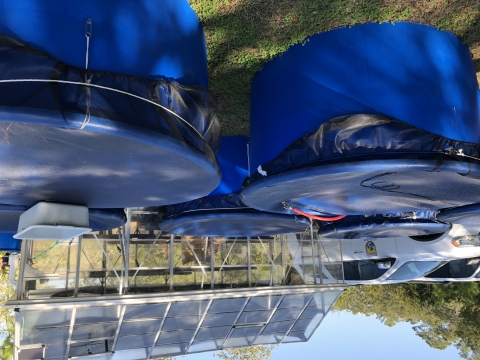 Tall blue plastic tanks sit above-ground on grass, covered with a plastic see-through textile. A greenhouse building and two vehicles are visible in the background.