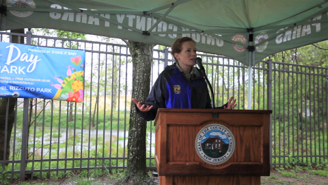 a woman speaking at a podium under a tent.