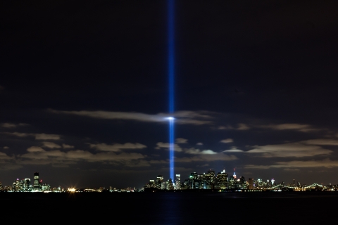 A bright beam of light reaching vertically into the sky from the New York City night skyline.