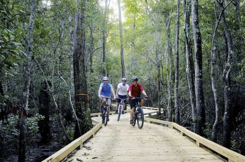 Three visitors biking on a wooden trail walkway at the Waccamaw National Wildlife Refuge.