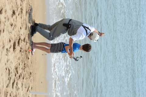 Surf casting volunteer assists child fishing on the beach
