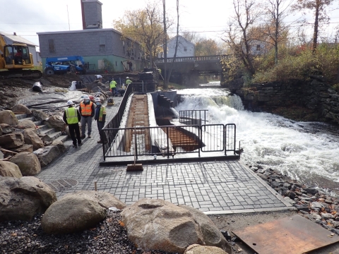 several workers stand near a dam and fish ladder as water rushes by