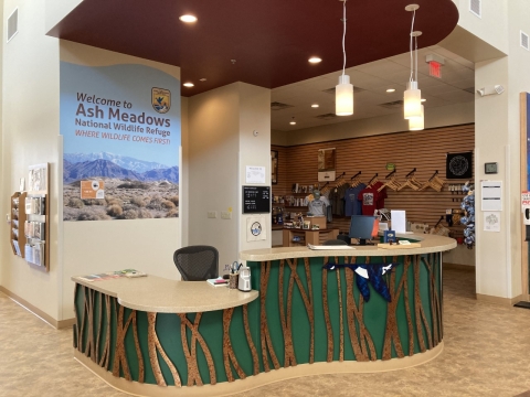 A desk with gift shop in the background, Sign that says "Welcome to Ash Meadows National Wildlife Refuge.