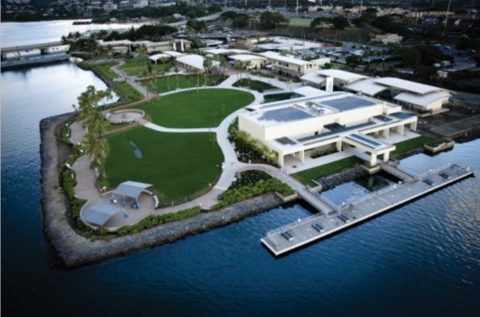 Aerial view of the Arizona Memorial. Water surrounds a lush, green lawn and white buildings. 