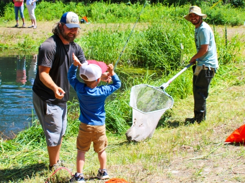 An excited boy beside a pond waves his arms to see his fish in a large net.