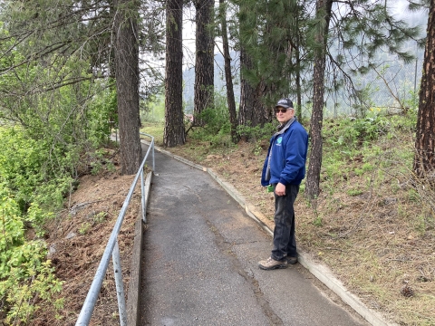 A man in ballcap and jacket stands on a newly cleaned trail.