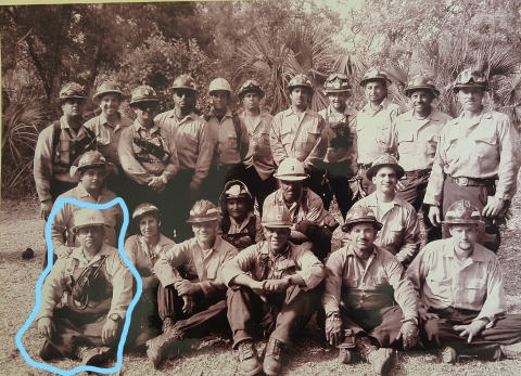 b&w photo of fire crew posing outdoors; person in front row on left circled
