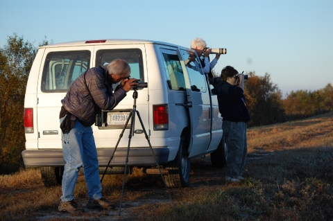 3 people using scopes & binoculars at white van looking for wildlife