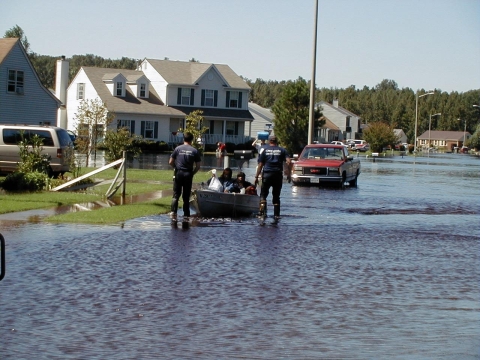 2 emergency workers pull a boat through flooded streets