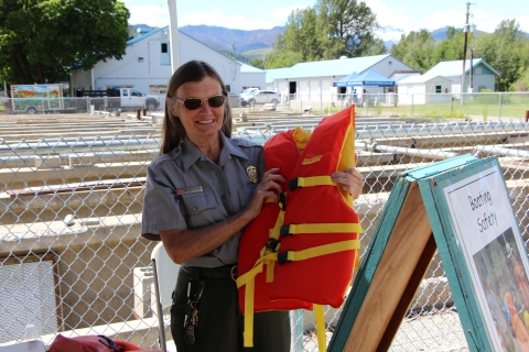 A uniformed woman in sunglasses smiles as she holds up a lifevest.