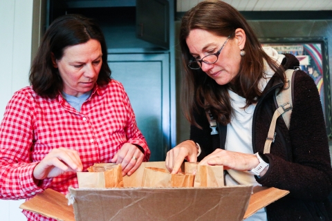 Two people stand over a box containing a number of paper bags.