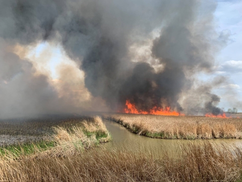 Fire on right and smoke above fields split with water