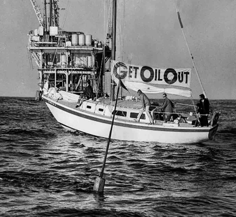 A black and white photo of a boat that has a sign that reads "Get Oil Out"