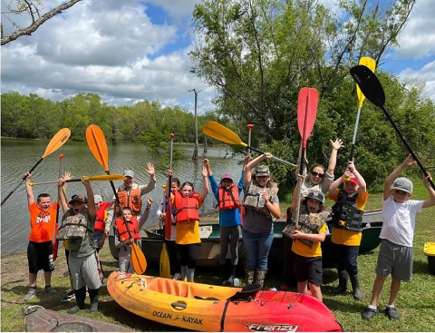 children hold up paddles next to a kayak