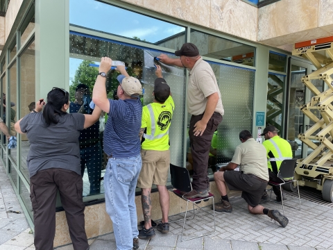 a group of people installing bird-friendly tape on a set of windows at a refuge.