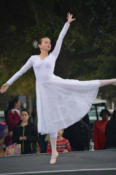 Brynn Garner wearing a white dress performs a ballet dance on a stage