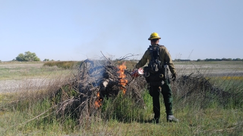 Firefighters with drip torch burns pile of debris on a hazy day