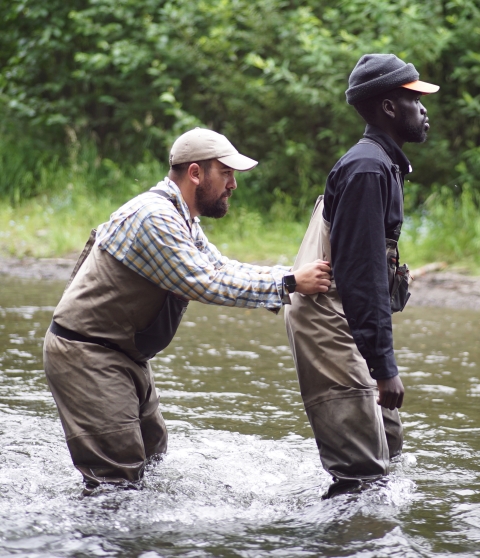 Two men shuffling carefully through a knee-deep river.