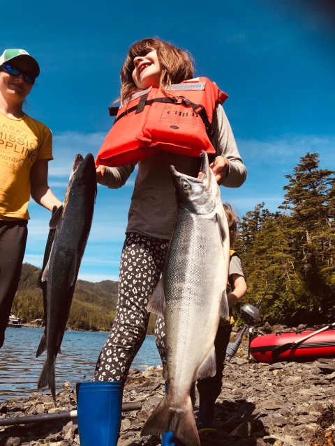 girl holds 2 salmon with mom in background