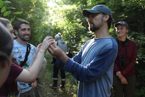 Biologist holds a small songbird up for a group of onlooking students