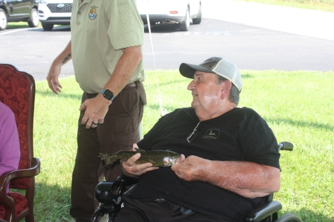 Elderly man in a wheelchair holding a rainbow trout.