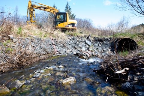 An excavator digs near an old and rusty culvert preparing to replace it in Kodiak, Alaska.