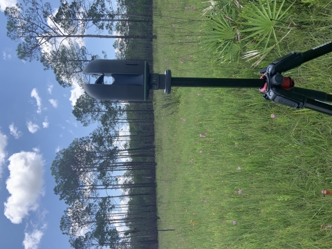 machine on tripod in meadow; trees in background