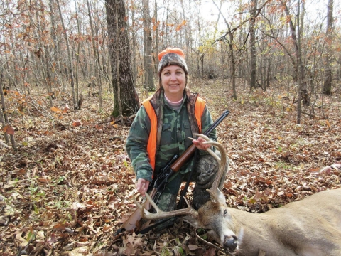 A hunter kneeling next to a buck kill laying on the ground in the forest