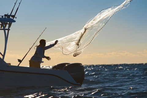 Man throws a fishing net off of a boat in the open water.