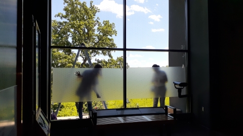 Two people apply window film on the outside of a large glass window