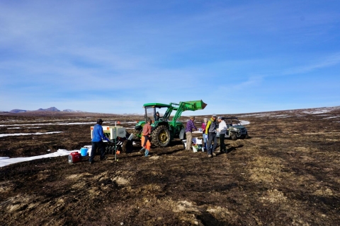 people standing around a green tractor on barren dirt 