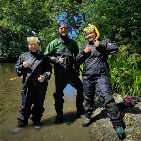 Two interns and a Service employee (middle), posing in a stream in their drysuits and snorkel gear prior to surveying the stream for fish estimates. 