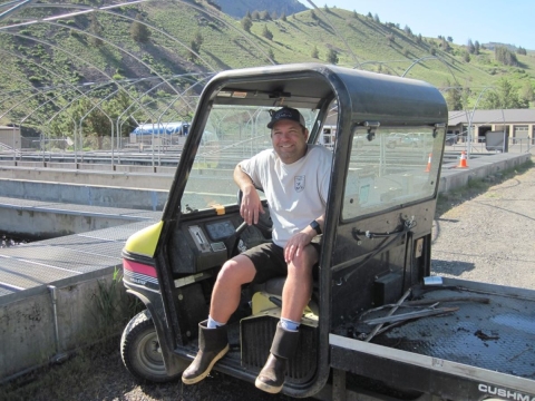 Steve Lazzini sitting in a OHV with hatchery raceways and rolling hills in the background