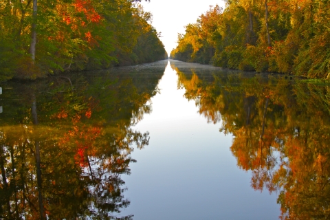 a glassy waterway reflects trees in fall foliage on both sides