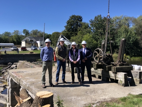 four people outside next to large metal gear 