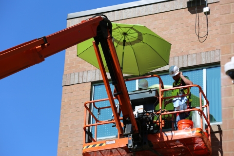 2 construction workers in construction uniform and hard hats on a boom lift next to a building window