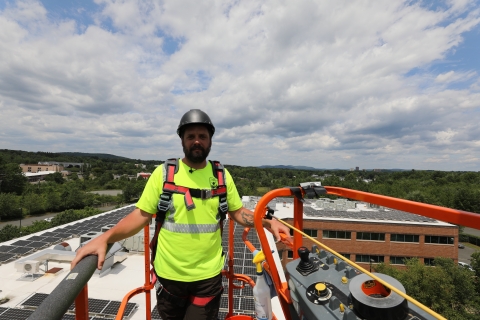 a man in construction attire stands up in the air on a boom lift above a large building.