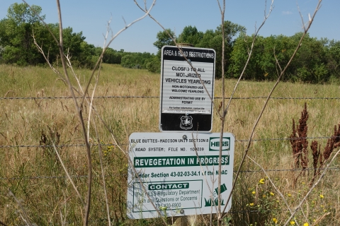 Two signs warn passersby that the grassland behind the fence is a Hess, Inc site that is closed for revegetation
