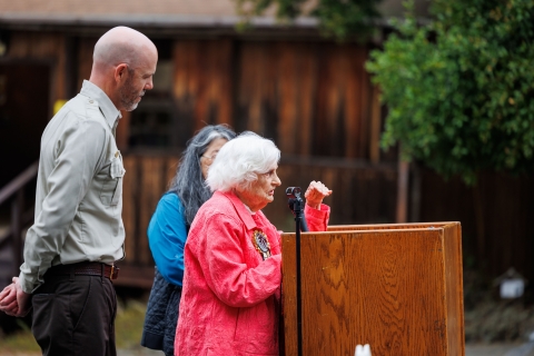 A woman stands at a podium, and two people stand alongside her