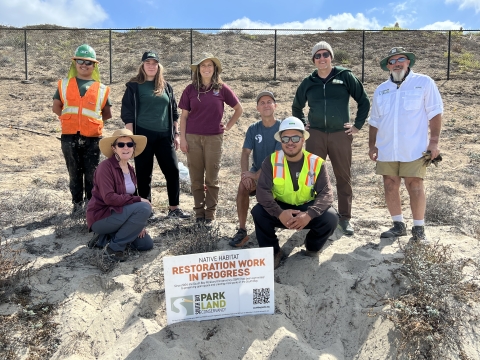 group of men and women posing on dune behind restoration work sign