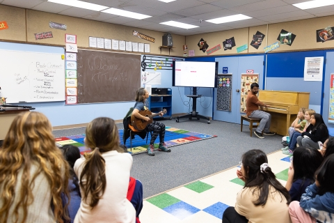 a woman plays guitar for children in a classroom
