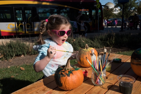 child sits at a table and paints pumpkins