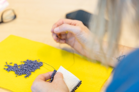 close up of hands sewing beads on a pouch