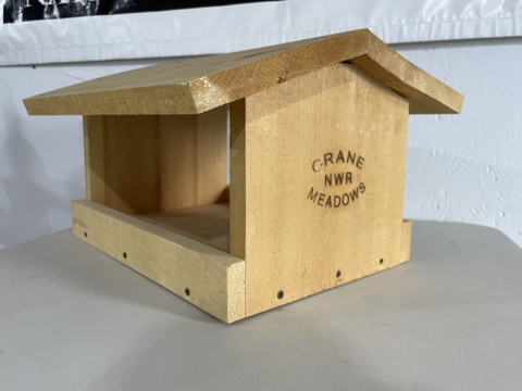 Wooden fly through bird feeder with Crane Meadows NWR branded on the wood