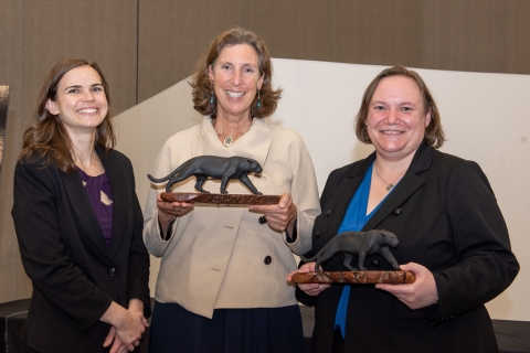 Three women smile at the camera, two holding small statues of jaguars