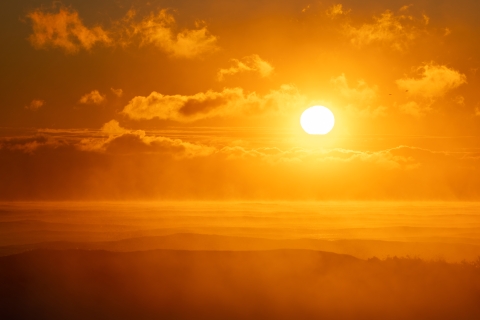 Image of the sun over clouds and a hazy landscape