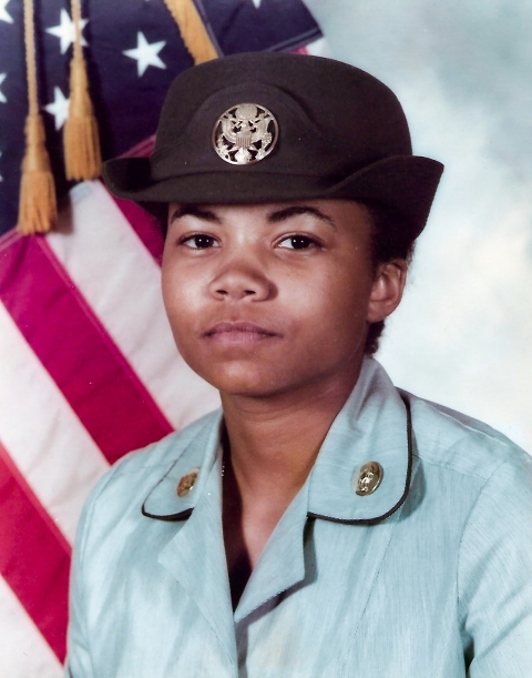 Portrait of a young U.S. Army soldier in a Class B uniform with US flag in the background.