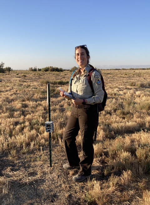 Kern National Wildlife Refuge biologist Katie Jimenez posing and smiling next to a wildlife camera trap attached to a stake